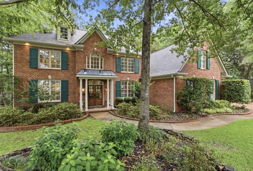 Traditional brick exterior featuring a covered entry, gabled roofline, multiple dormer windows, and dark green louvered shutters