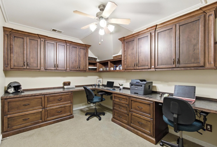 Dedicated workspace featuring extensive built-in wood cabinetry, integrated desk surfaces, and a ceiling fan with light fixture