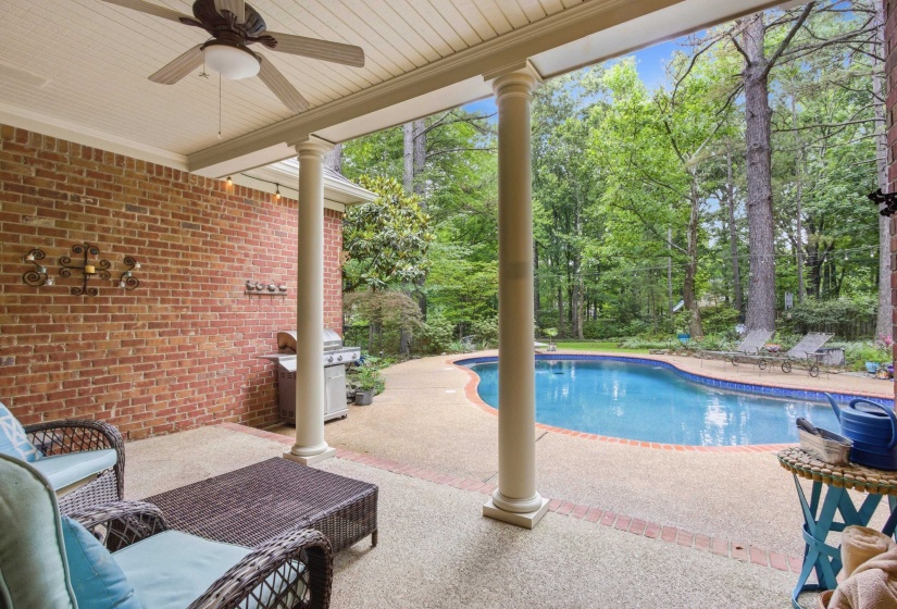Covered patio with a ceiling fan, brick accent wall, and exposed aggregate concrete flooring