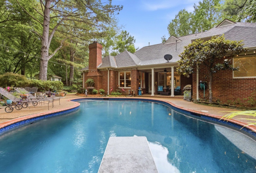Curved inground pool with a diving board, surrounded by a textured concrete pool deck