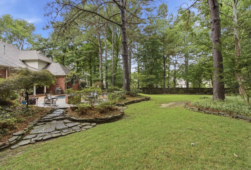 Spacious backyard featuring a lush lawn, mature trees, and a stone-edged planting bed