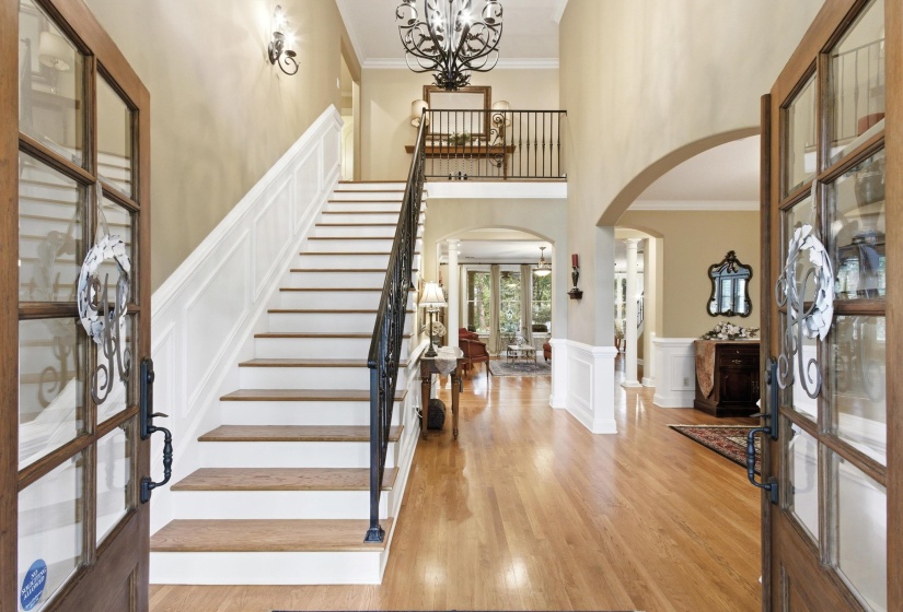 Two-story foyer featuring a grand staircase with wood-finish treads, white risers, and a wrought iron railing
