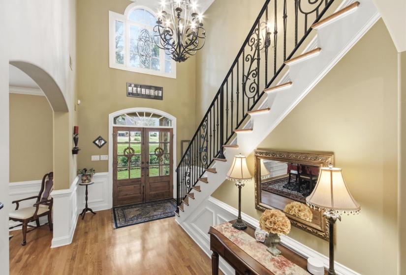 Two-story foyer featuring an arched entryway, natural wood-finish flooring, and a grand staircase with wrought iron balusters