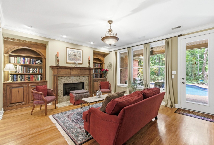 Living area featuring hardwood flooring, a fireplace with a stone surround and wood mantel, and built-in arched bookcases