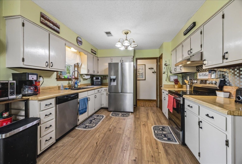 Spacious kitchen featuring extensive white cabinetry, wood-finish countertops, and a modern stainless steel appliance suite including a refrigerator, dishwasher, and range