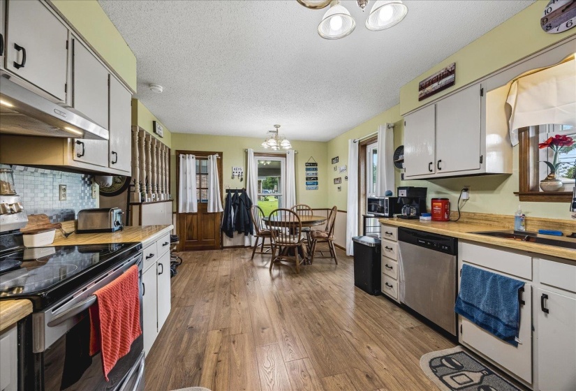 Kitchen featuring wood-finish flooring, white cabinetry, integrated stainless steel appliances, light-toned countertops, and a tiled backsplash