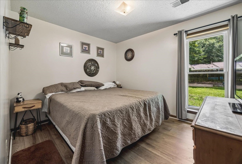 Bedroom featuring wood-finish flooring, neutral wall paint, and a window with direct backyard access