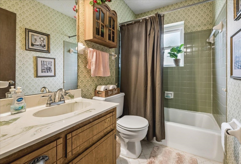 Bathroom featuring a white vanity with an integrated sink, a built-in toilet, and a white bathtub with green subway tile surround