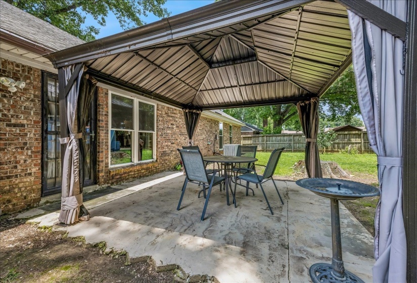 Expansive stamped concrete patio featuring a permanent gazebo structure with a hardtop roof and privacy curtains