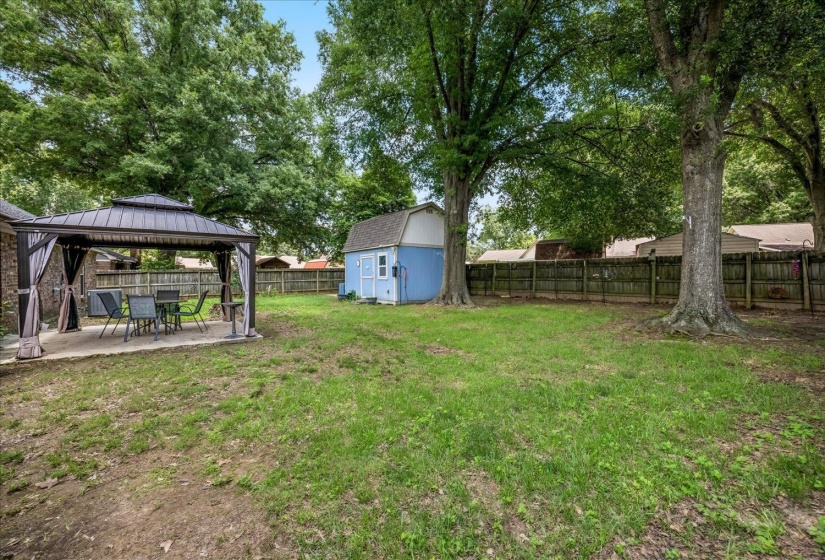 Expansive backyard featuring a covered patio with a metal gazebo, a detached storage shed, a wood privacy fence, and mature trees