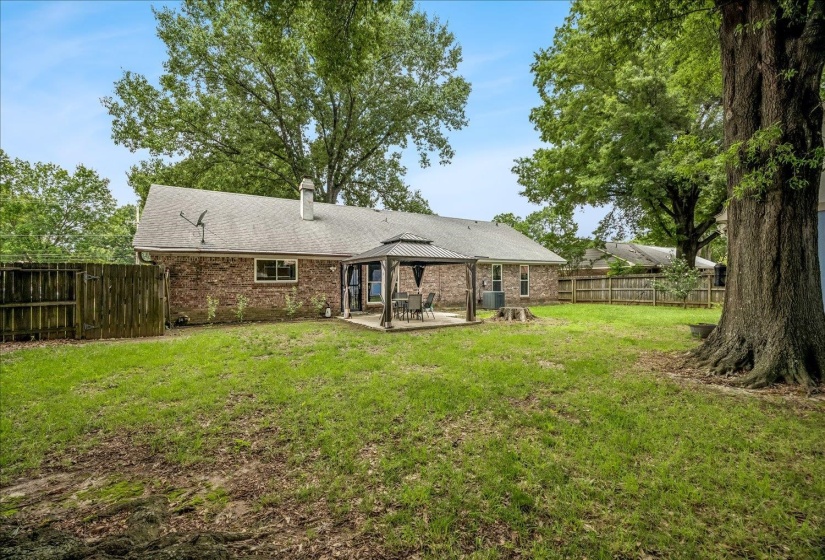 Spacious backyard featuring a brick exterior, a covered patio, mature trees, a privacy fence, and a generous lawn area