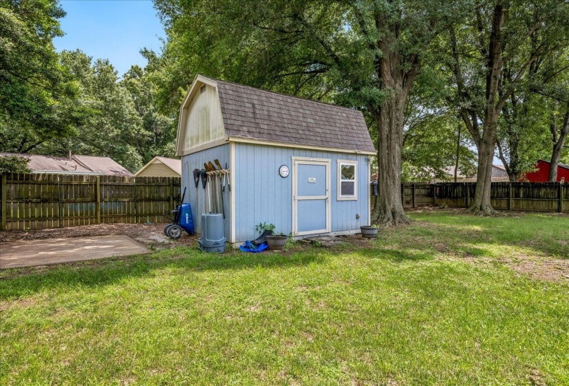 Detached blue storage shed with gambrel roof and a fenced perimeter