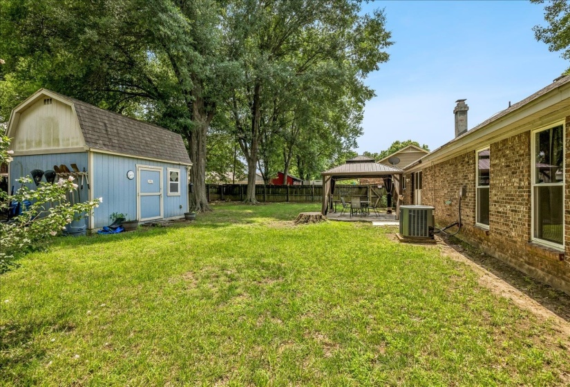 Expansive green lawn featuring a blue storage shed, mature trees, and a covered patio area with a gazebo