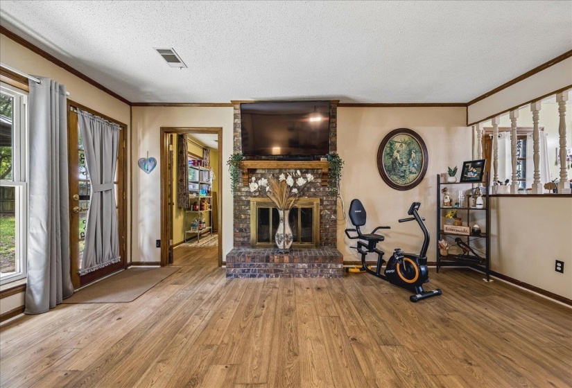 Living area featuring wood-finish flooring, a brick fireplace with a wood mantle, and a glass-paneled door opening to outdoor space
