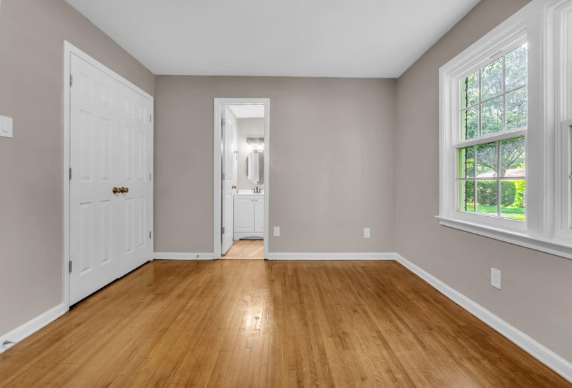 Hardwood flooring complemented by neutral wall tones, a double-door closet, and a multi-pane window with white trim