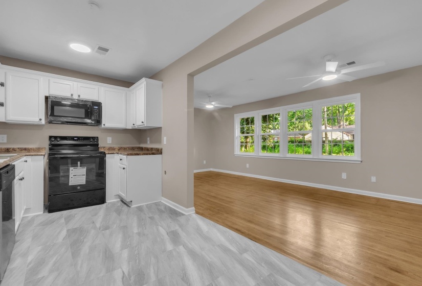 Open-concept kitchen and living area featuring white cabinetry, black appliances, and durable wood-finish flooring