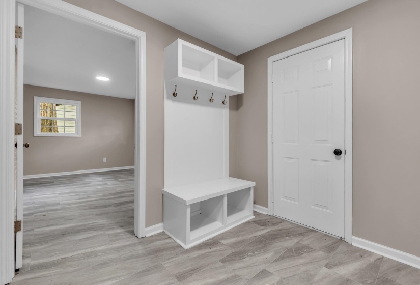 Entryway featuring a built-in white mudroom bench with storage cubbies and upper shelving, coat hooks, and durable wood-finish flooring