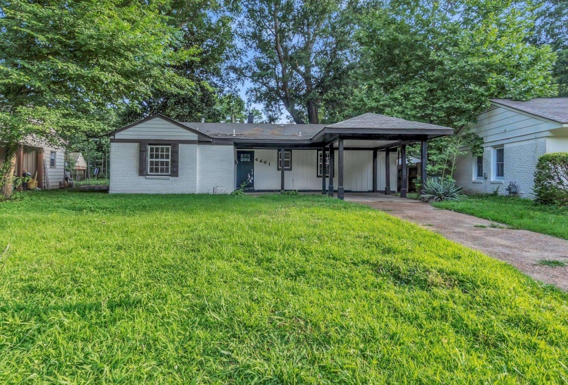 White brick exterior with a dark trim roofline, an attached carport, and a front lawn with mature trees
