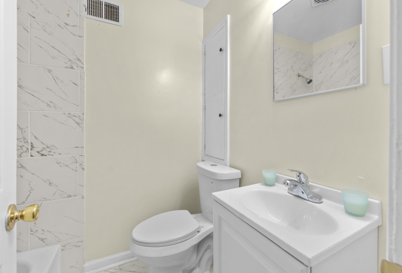 Bathroom featuring a white vanity with integrated sink, chrome faucet, wall-mounted mirror, and white tiled shower surround