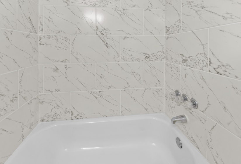 Bathtub featuring white tile surround with gray veining and chrome fixtures