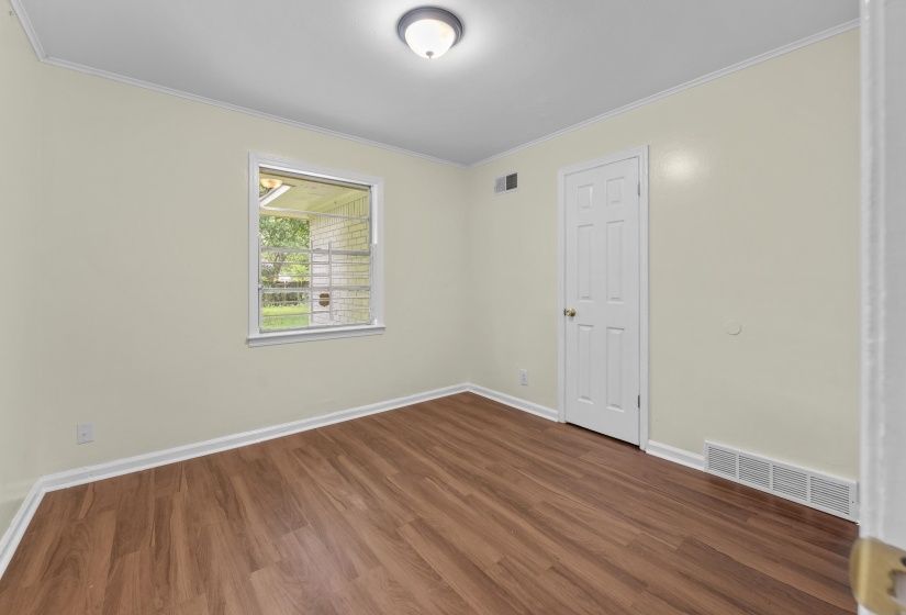 Interior room featuring wood-finish flooring, white baseboards, and a single window with exterior landscaping visible