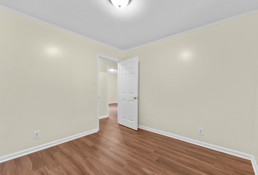 Interior space featuring wood-finish flooring, light-toned walls, white baseboards, and white crown molding