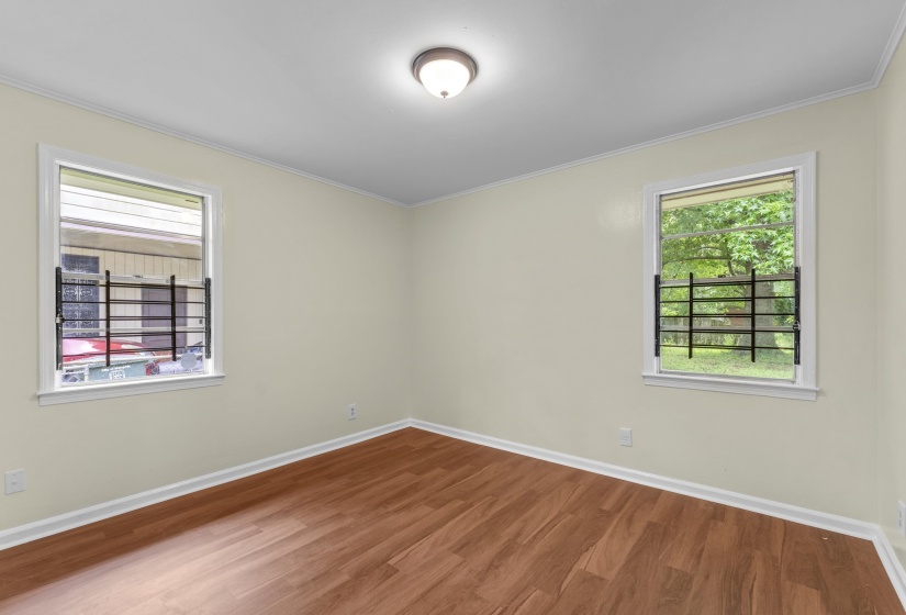 Neutral wall finishes complement the wood-finish flooring in this room featuring two windows with security bars