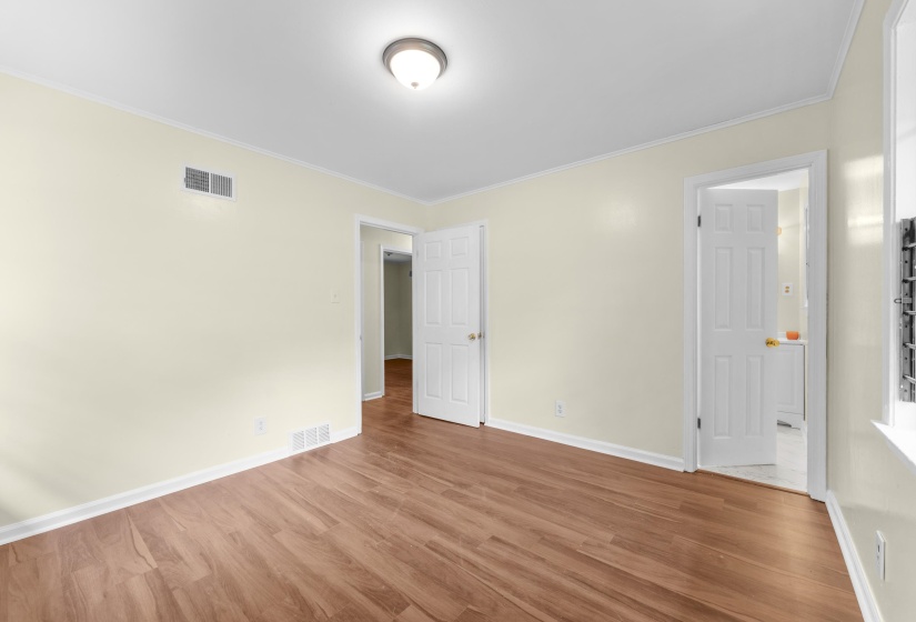 Neutral-toned room featuring wood-finish flooring, white baseboards, and crown molding