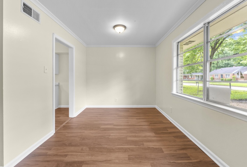 Spacious room featuring wood-finish flooring, light cream wall paint, white baseboards, crown molding, and a large multi-pane window