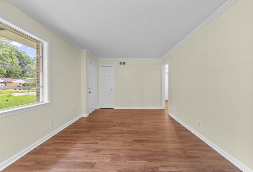 Spacious room featuring wood-finish flooring, light-toned walls, white crown molding, and a large window