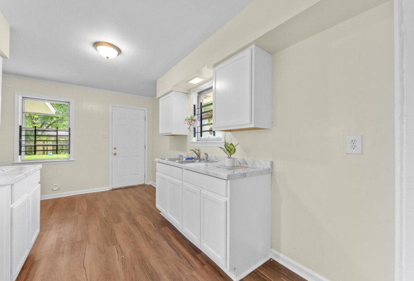 Kitchen featuring wood-finish flooring, white cabinetry, a double basin sink, and light-toned countertops
