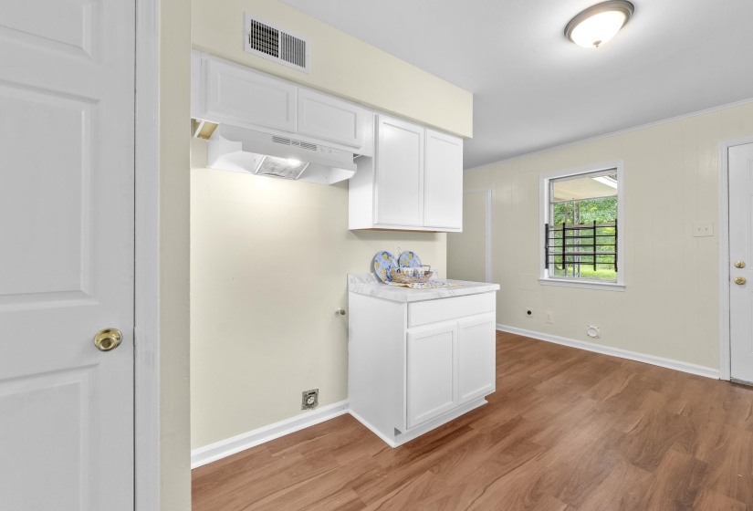 Compact kitchen area featuring white cabinetry, a light-toned countertop, and wood-finish flooring