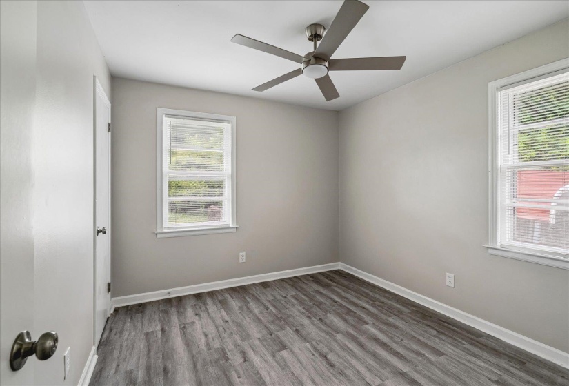 Spacious room featuring wood-finish flooring, light gray walls, two windows with blinds, a modern ceiling fan, and white trim