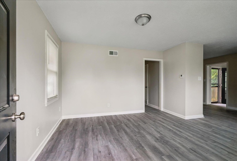Spacious room featuring wood-finish flooring, light neutral wall tones, white trim, and a ceiling-mounted light fixture