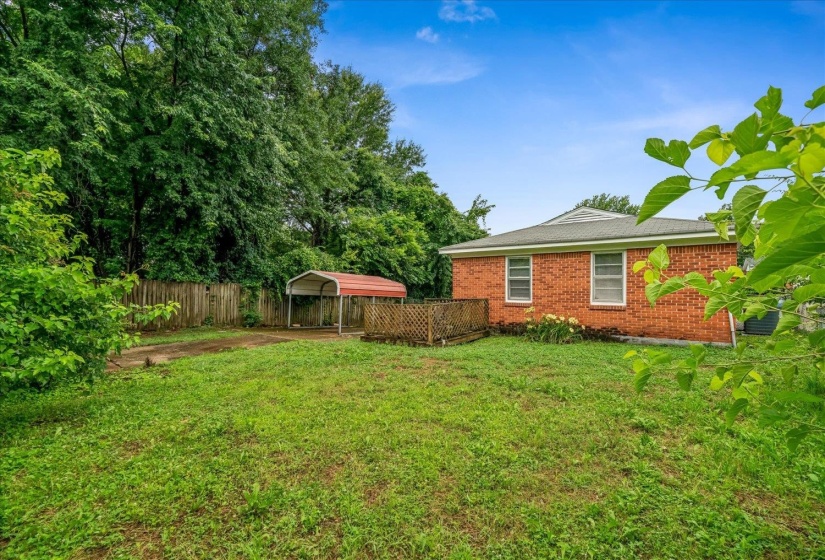 Expansive backyard featuring a red brick exterior, metal roof, wood deck, and a detached carport