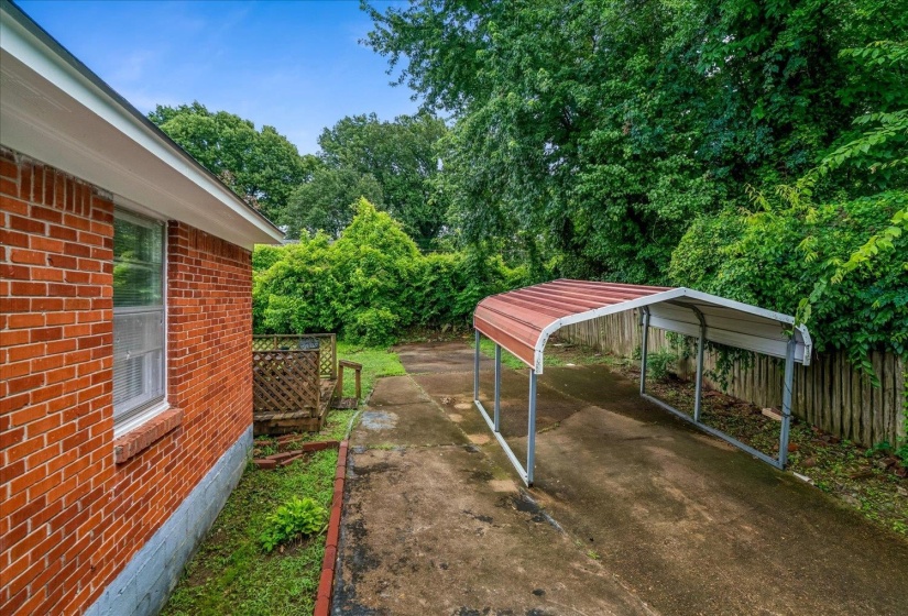 Exterior featuring brick siding, a window with a screen, a carport with a metal roof, a concrete driveway, and mature landscaping