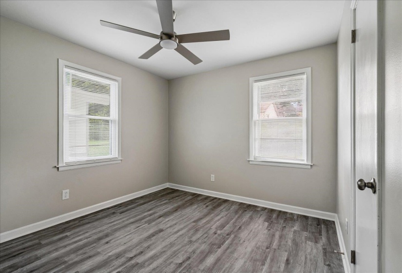 Room featuring wood-finish flooring, two large windows with blinds, a ceiling fan, and neutral wall paint