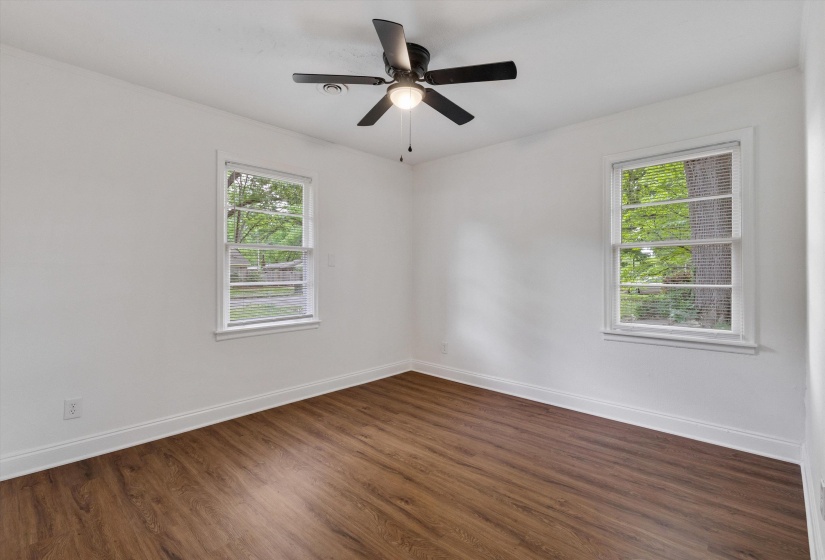 Spacious room featuring two windows with white trim, wood-finish flooring, white walls, and a ceiling fan with light fixture