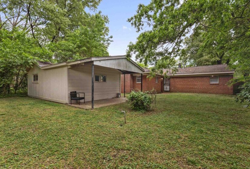 Spacious backyard featuring a detached outbuilding with covered patio, brick exterior home, and mature trees