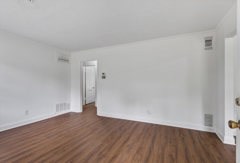 Spacious room featuring wood-finish flooring, white walls, and crown molding