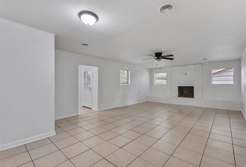 Spacious living area featuring neutral-toned floor tiling, a painted brick fireplace, white walls, and multiple windows