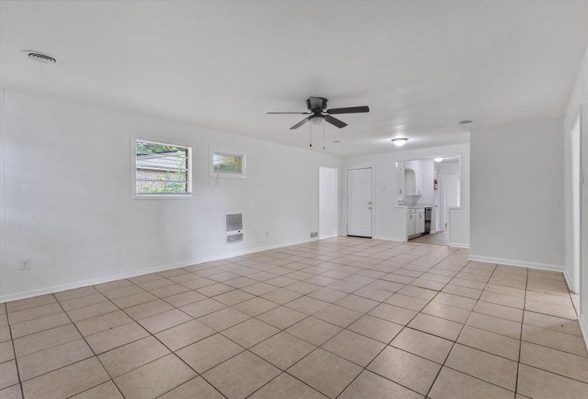 Spacious interior room featuring light-toned square tile flooring, a dark-toned ceiling fan, and white walls
