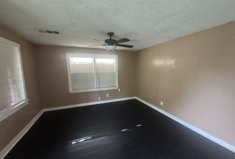 Spacious room featuring dark-stained wood flooring, two windows with blinds, a ceiling fan with light fixture, and neutral-toned walls