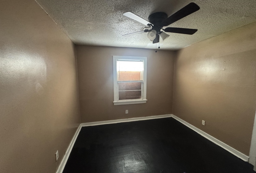 Room featuring a ceiling fan with light fixture, single window, dark flooring, and light brown wall paint
