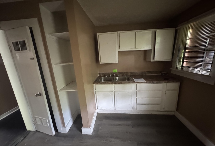 Compact kitchen area featuring a double basin stainless steel sink, white cabinetry with storage drawers, and a window with blinds