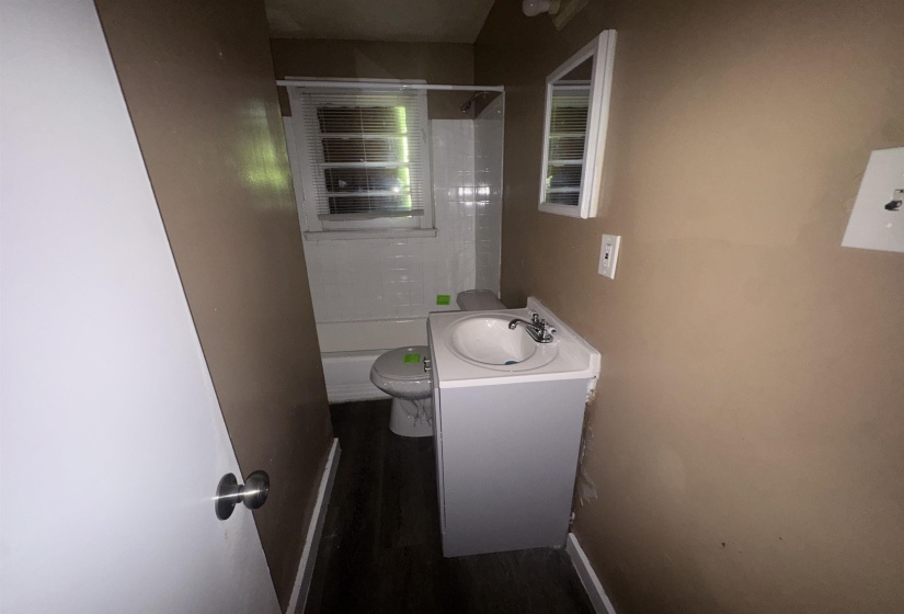 Bathroom featuring a white vanity with integrated sink, chrome faucet, wall-mounted mirror, and dark wood-finish flooring