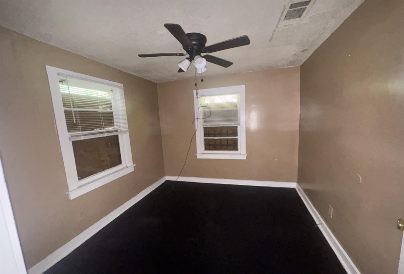 Room featuring two windows with white blinds, black flooring, a ceiling fan with integrated lighting, and beige wall paint