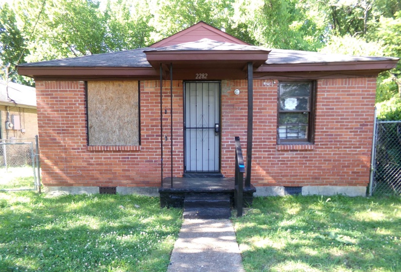 Brick facade home featuring a covered front entry, concrete pathway, and mature trees in the background