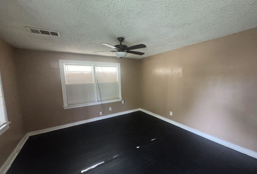 Spacious room featuring dark wood-finish flooring, light tan walls, and a white popcorn ceiling