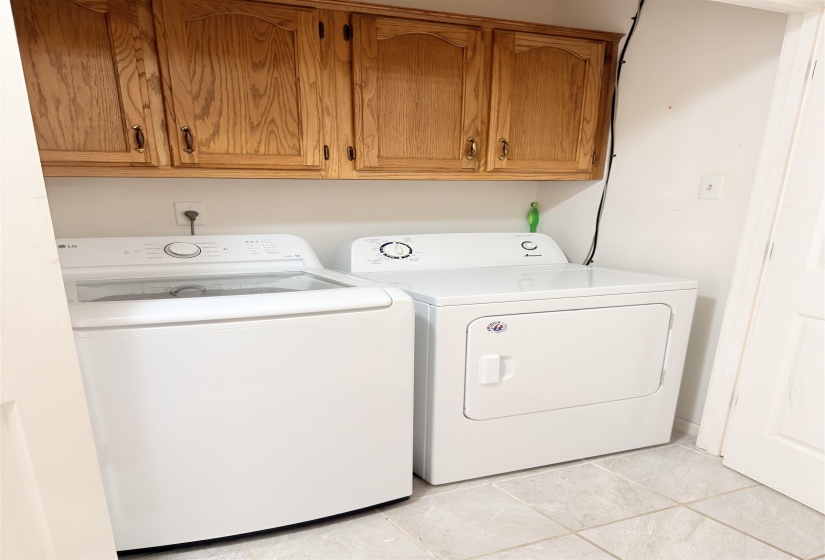 Laundry area featuring light wood cabinetry with dark hardware, a white top-load washing machine, a white electric dryer, and light-toned square tile flooring